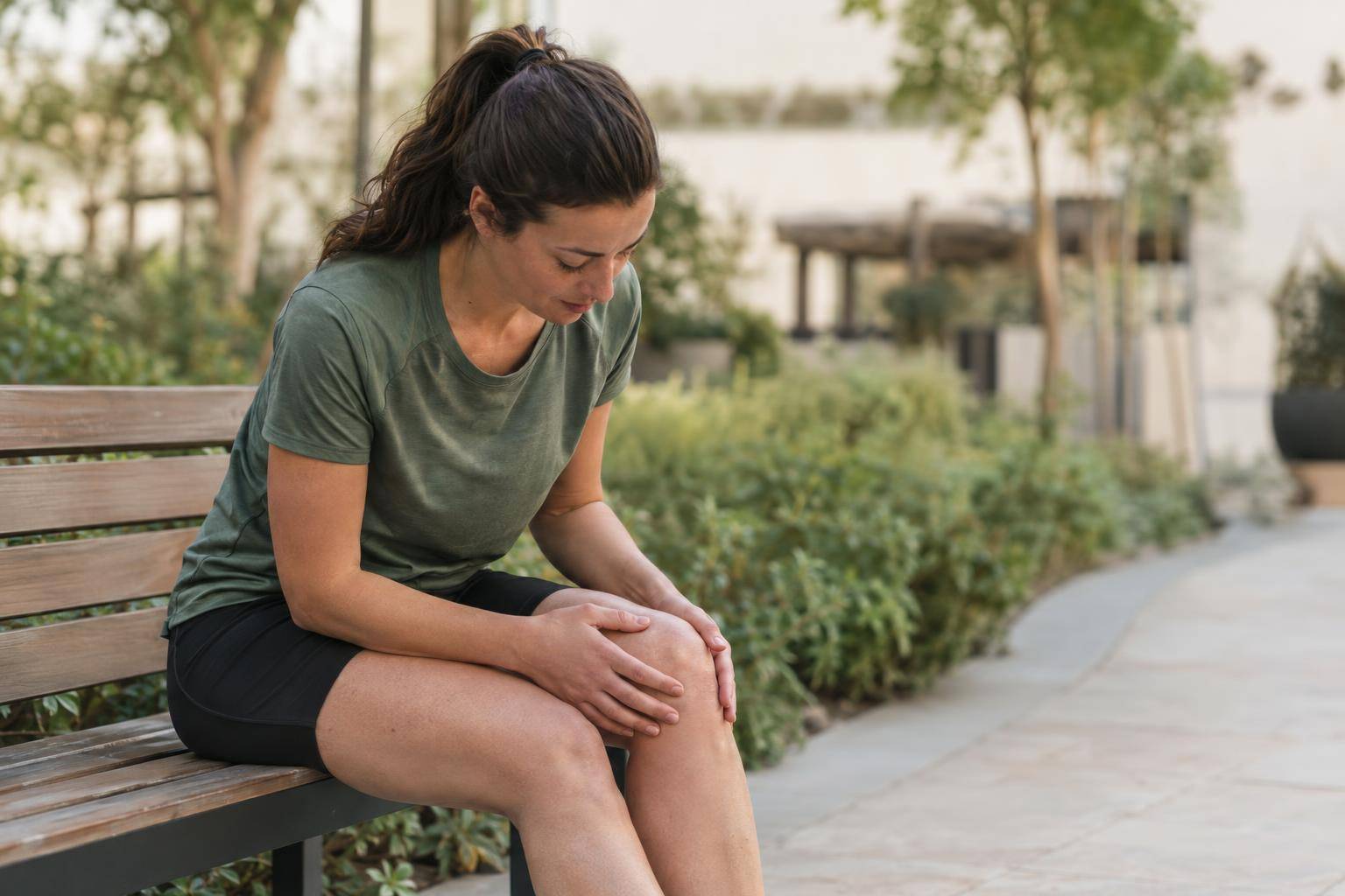 A person sits on a bench beside a path and checks their knee after jogging