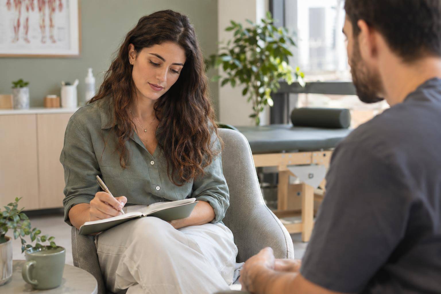 A patient writes questions in a notebook while seated in a consultation room