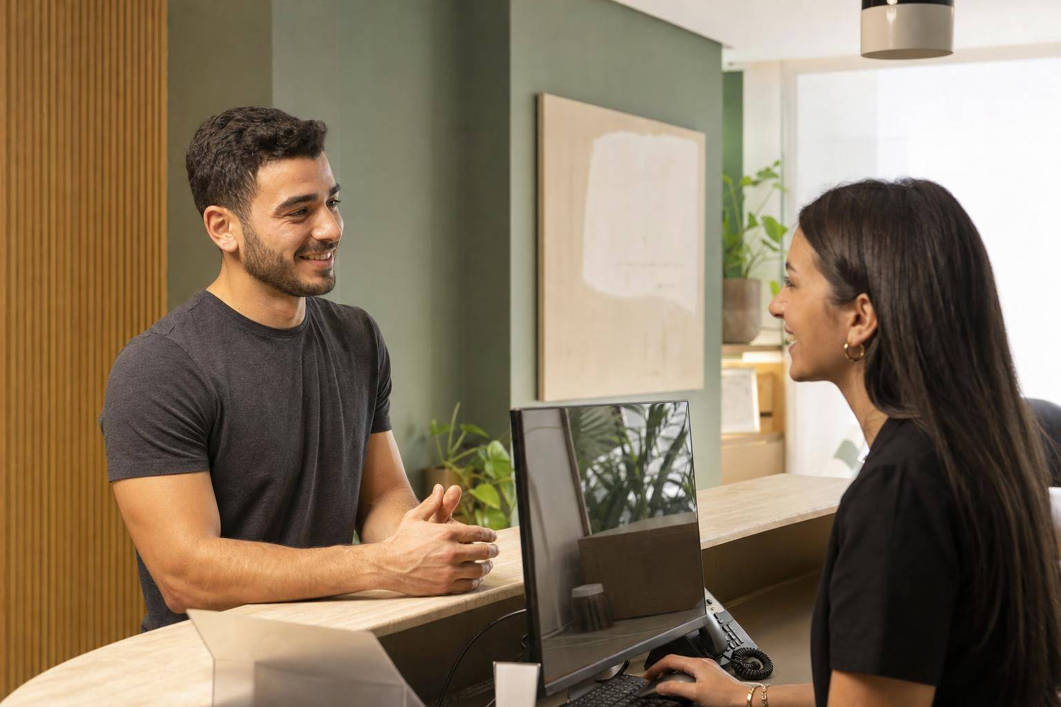 Patient and clinic administrator discuss insurance coverage at a reception desk before booking